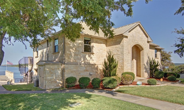 view of front of home featuring central AC unit, a standing seam roof, a front lawn, stone siding, and metal roof