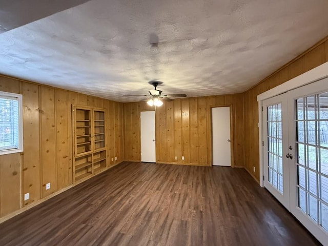 spare room featuring a ceiling fan, dark wood-style floors, baseboards, and wood walls