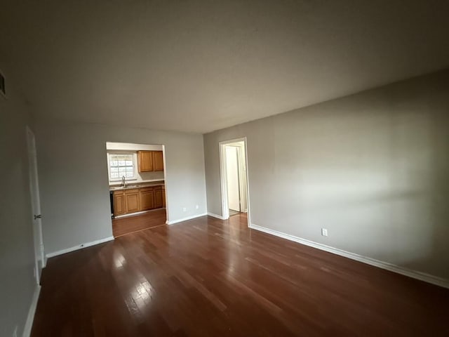 unfurnished living room featuring baseboards, dark wood-style flooring, and a sink