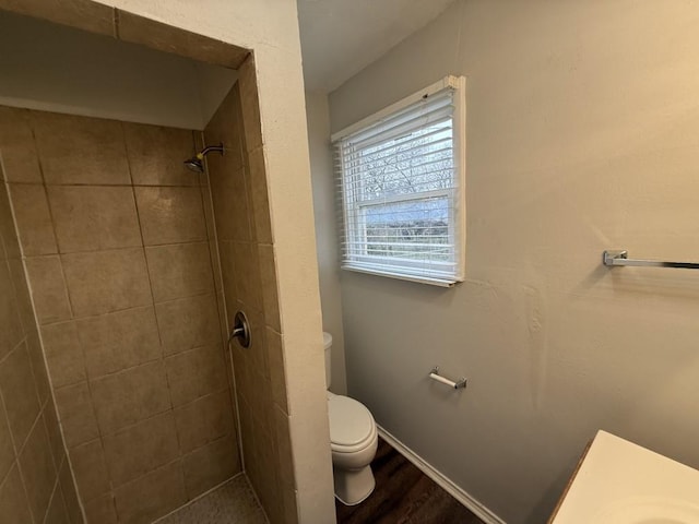 full bathroom with toilet, wood finished floors, baseboards, and tiled shower