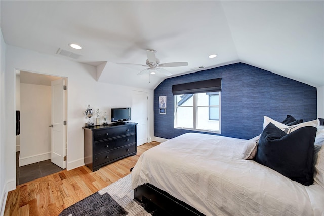 bedroom with visible vents, an accent wall, lofted ceiling, and wood finished floors