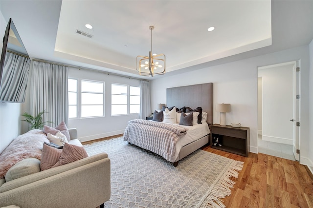 bedroom with a raised ceiling, light wood-style floors, visible vents, and a chandelier