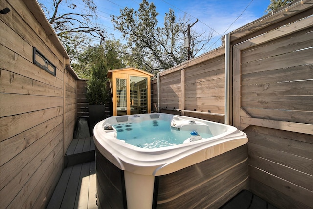 wooden terrace with an outdoor structure, fence private yard, and a hot tub