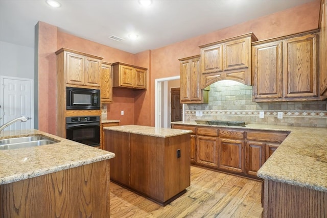 kitchen with light wood finished floors, visible vents, a kitchen island, black appliances, and a sink