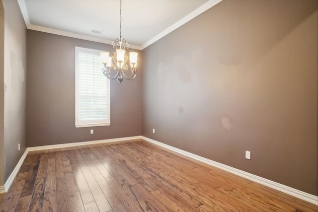 spare room with visible vents, a notable chandelier, ornamental molding, wood finished floors, and baseboards