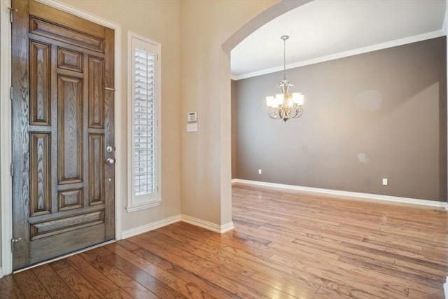 entryway with light wood finished floors, arched walkways, baseboards, and ornamental molding