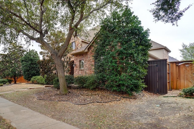 view of side of home featuring brick siding, a shingled roof, and fence