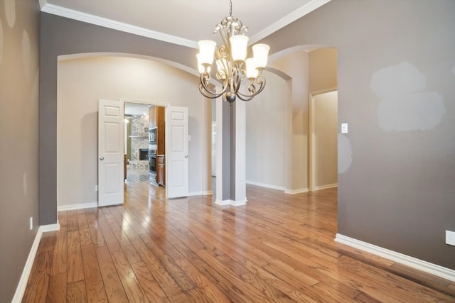 unfurnished dining area featuring baseboards, arched walkways, ornamental molding, and light wood finished floors