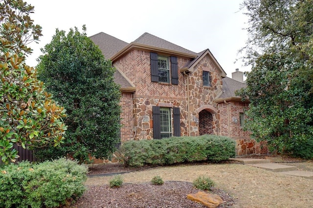 view of front of property with brick siding, stone siding, a chimney, and a shingled roof