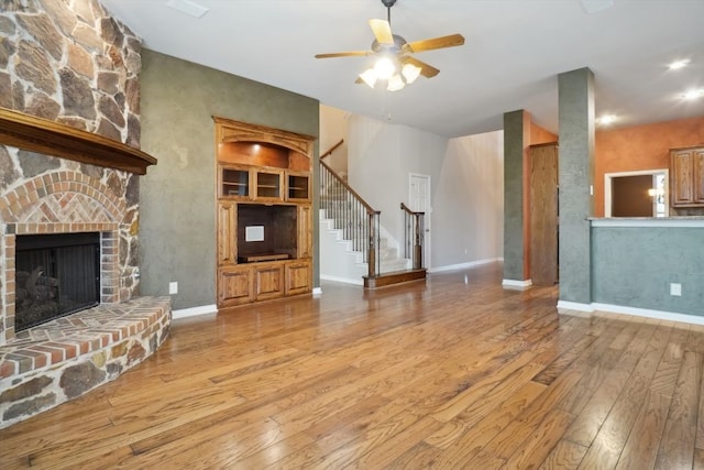 unfurnished living room featuring stairway, baseboards, ceiling fan, hardwood / wood-style flooring, and a large fireplace