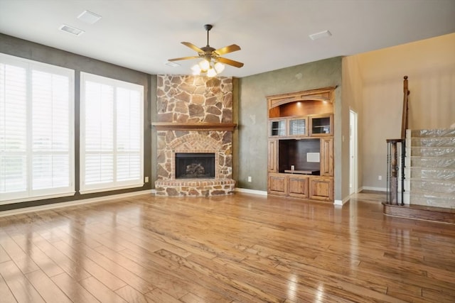 unfurnished living room featuring a fireplace, wood finished floors, baseboards, and ceiling fan