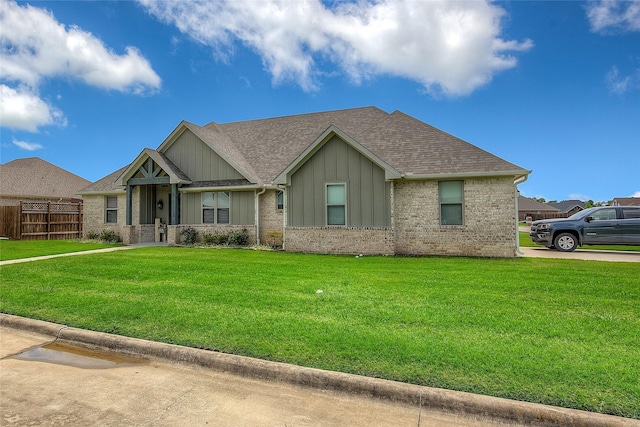 view of front of property with a front lawn, fence, board and batten siding, a shingled roof, and brick siding