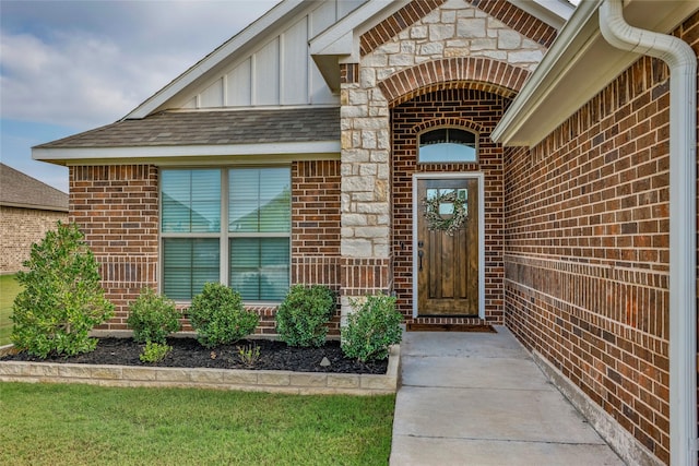 view of exterior entry featuring brick siding, board and batten siding, stone siding, and roof with shingles