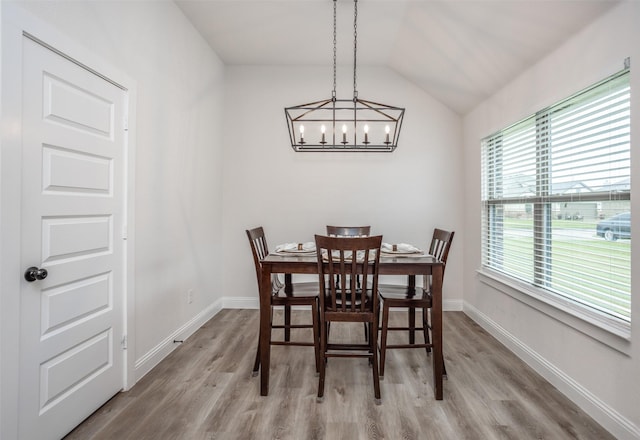 dining area featuring a chandelier, light wood-style flooring, baseboards, and vaulted ceiling