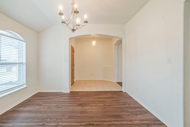 unfurnished dining area with a notable chandelier, lofted ceiling, wood finished floors, arched walkways, and baseboards