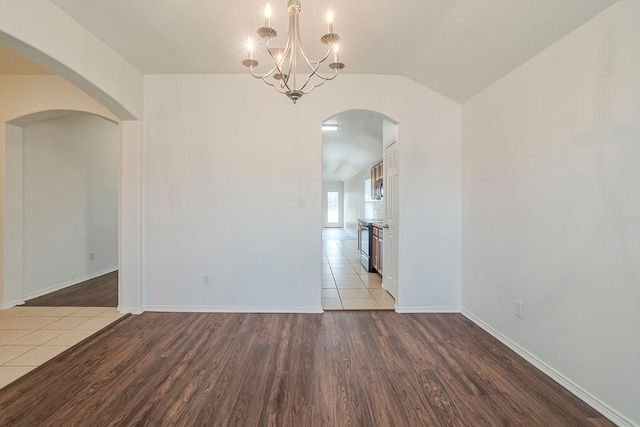 empty room featuring vaulted ceiling, wood finished floors, arched walkways, and a chandelier