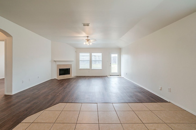 unfurnished living room with wood finished floors, visible vents, arched walkways, ceiling fan, and a tiled fireplace