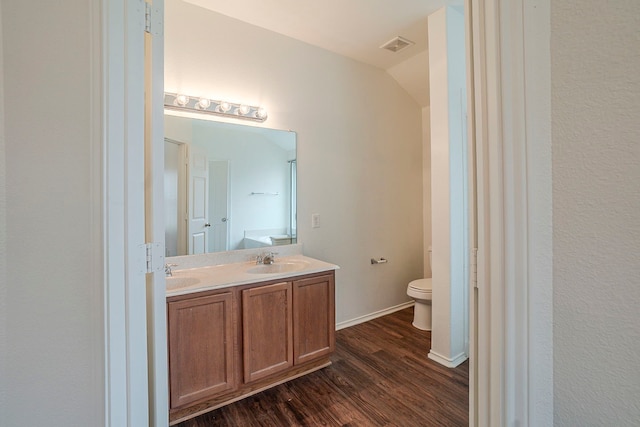 bathroom with visible vents, toilet, a sink, wood finished floors, and double vanity