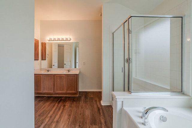 full bath with wood finished floors, double vanity, a sink, a shower stall, and a garden tub