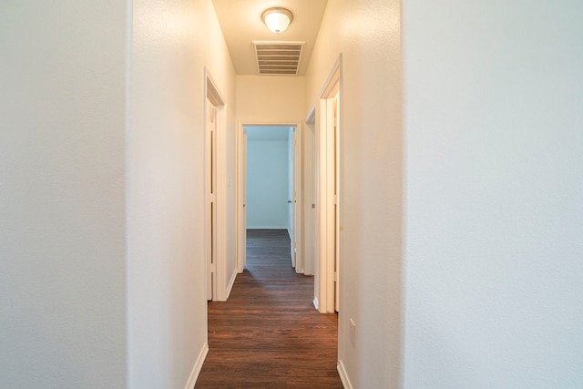 hall with visible vents, baseboards, and dark wood-style floors