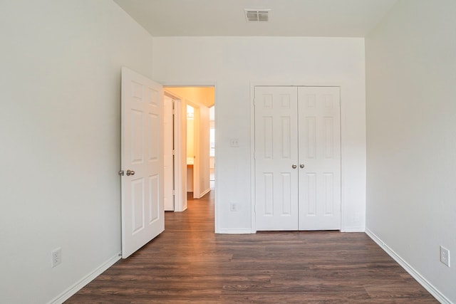 unfurnished bedroom with dark wood finished floors, baseboards, visible vents, and a closet