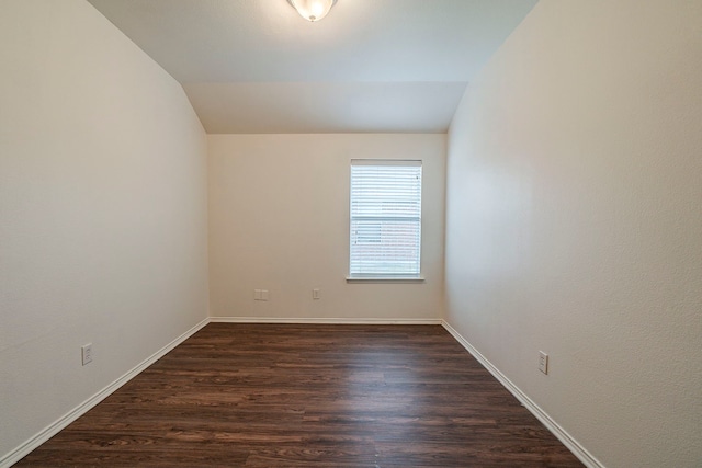 empty room featuring lofted ceiling, dark wood-style floors, and baseboards