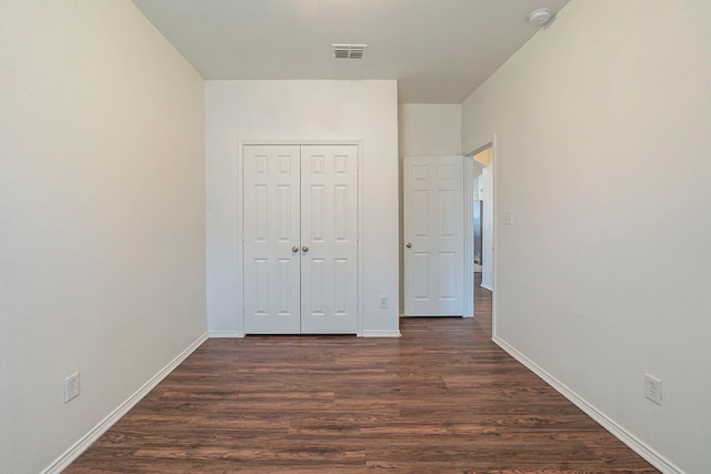 unfurnished bedroom with a closet, baseboards, visible vents, and dark wood-style flooring