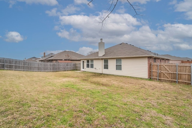 rear view of house with a yard, a fenced backyard, and a chimney