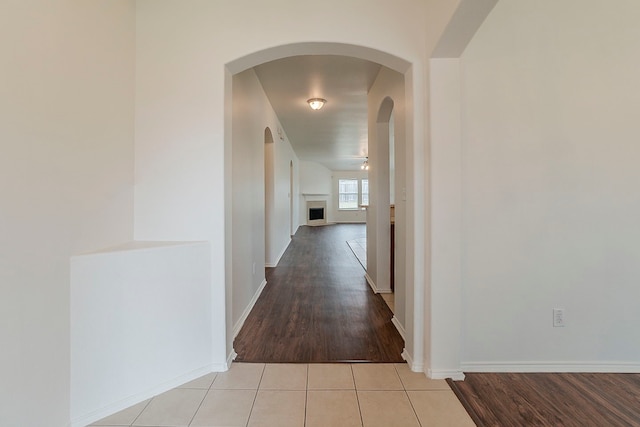 hall with light tile patterned flooring, arched walkways, and baseboards