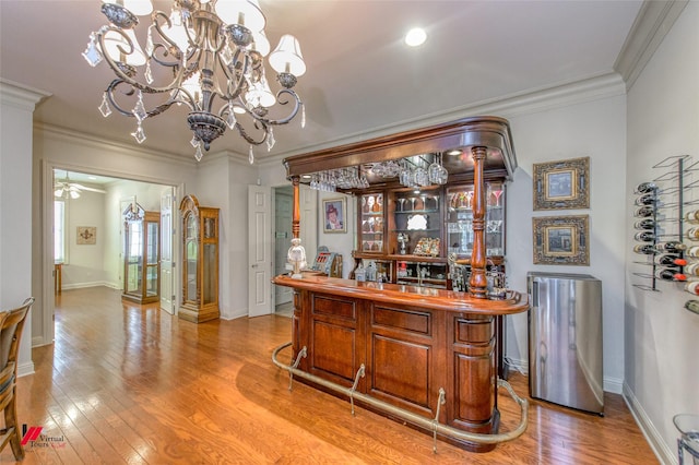 bar featuring a ceiling fan, light wood-style floors, a bar, crown molding, and baseboards