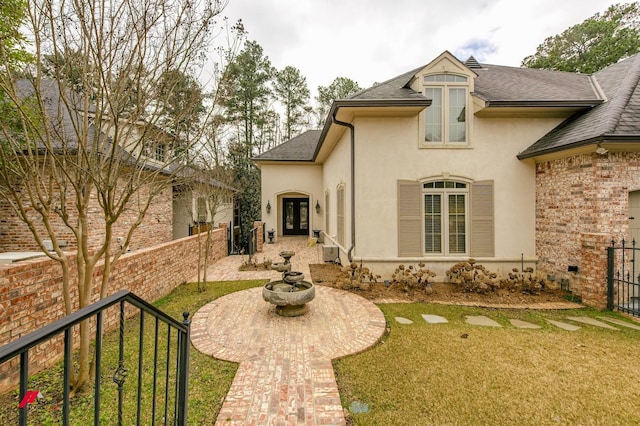 rear view of property featuring stucco siding, a lawn, fence, french doors, and a shingled roof