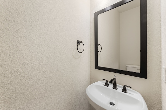 bathroom with toilet, a textured wall, and a sink