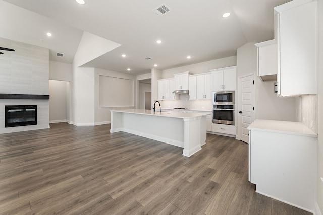 kitchen featuring built in microwave, a sink, decorative backsplash, under cabinet range hood, and stainless steel oven