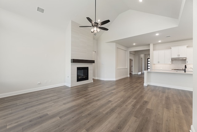 unfurnished living room with visible vents, dark wood-type flooring, high vaulted ceiling, ceiling fan, and a tile fireplace