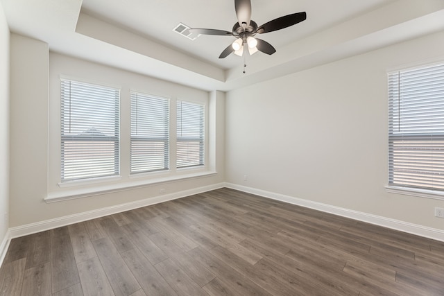 unfurnished room with dark wood finished floors, a ceiling fan, a raised ceiling, and baseboards