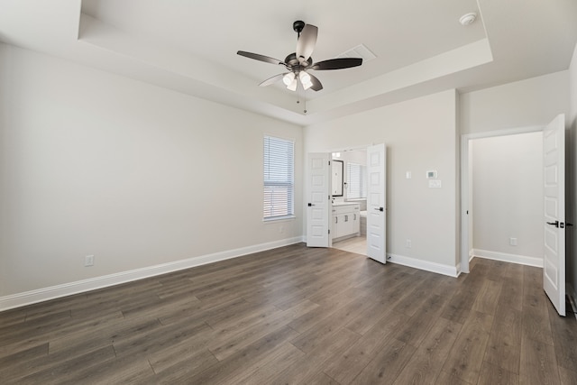 unfurnished bedroom with a raised ceiling, baseboards, dark wood-type flooring, and connected bathroom