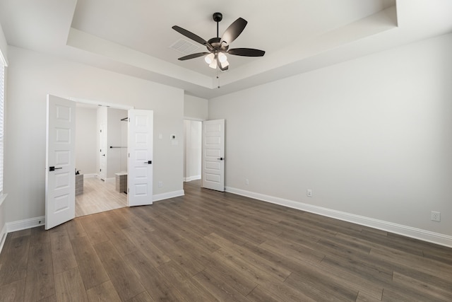 unfurnished bedroom featuring visible vents, dark wood-type flooring, ceiling fan, baseboards, and a tray ceiling