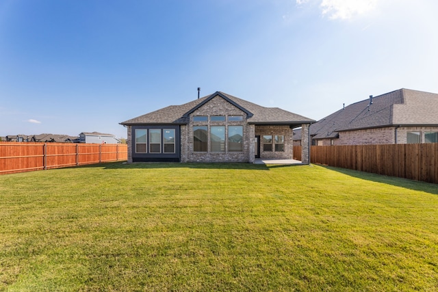 rear view of property with brick siding, a lawn, a shingled roof, and a fenced backyard