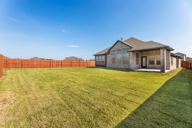 rear view of property featuring roof with shingles, a yard, a fenced backyard, a patio area, and brick siding