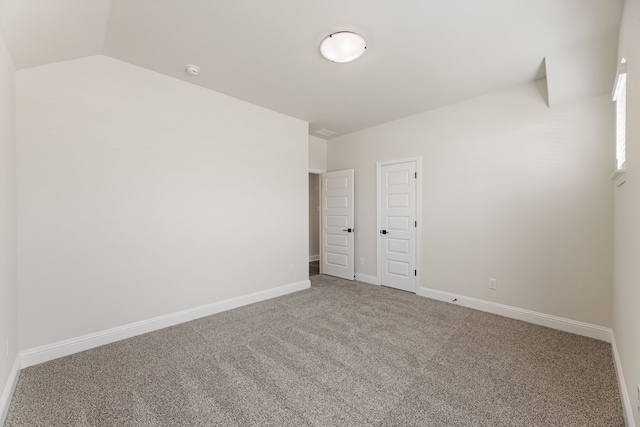 carpeted spare room featuring lofted ceiling and baseboards