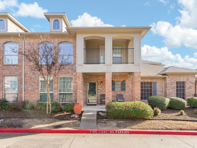 multi unit property featuring a balcony, brick siding, and roof with shingles