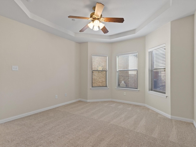 unfurnished room featuring a raised ceiling, light colored carpet, baseboards, and ceiling fan