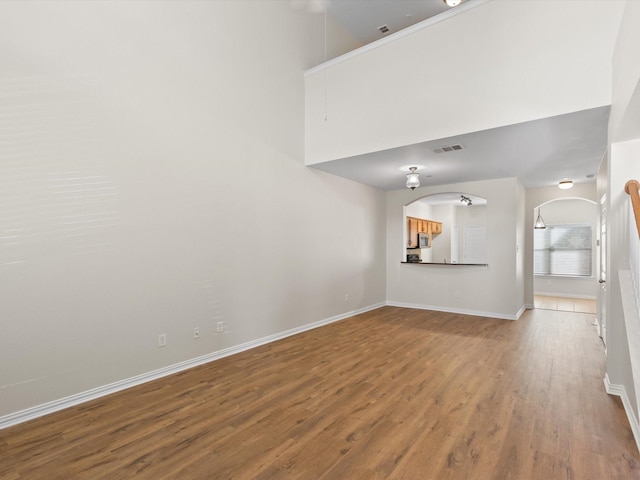 unfurnished room featuring arched walkways, visible vents, baseboards, and wood finished floors