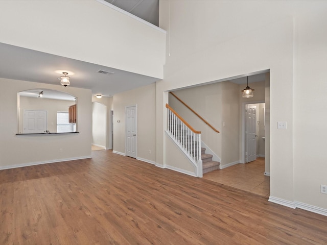 unfurnished living room with arched walkways, visible vents, stairway, and wood finished floors