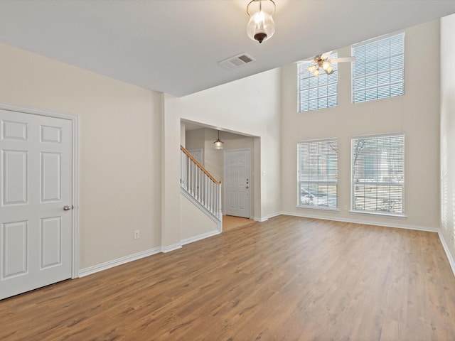 unfurnished living room with visible vents, baseboards, wood finished floors, and stairs