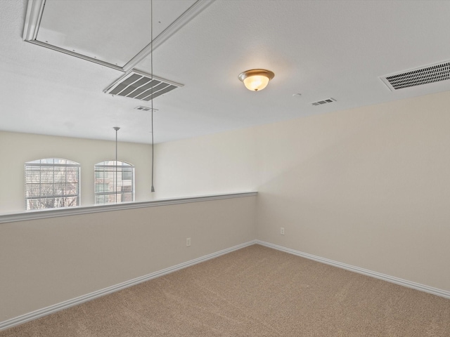 carpeted empty room with visible vents, baseboards, and attic access