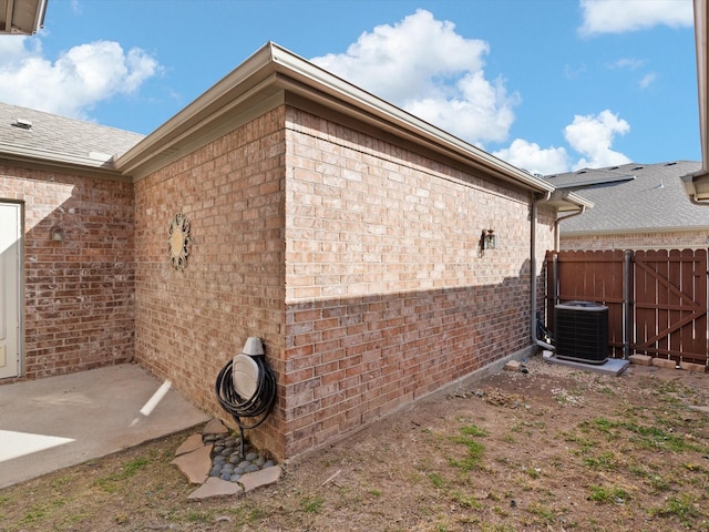 view of side of property featuring cooling unit, brick siding, and fence