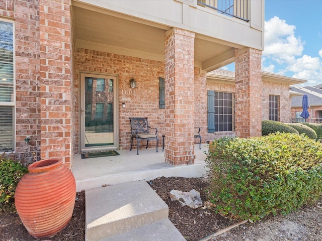 property entrance with brick siding, a porch, and a balcony