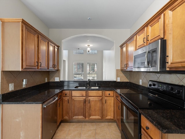 kitchen with brown cabinetry, appliances with stainless steel finishes, arched walkways, light tile patterned flooring, and a sink