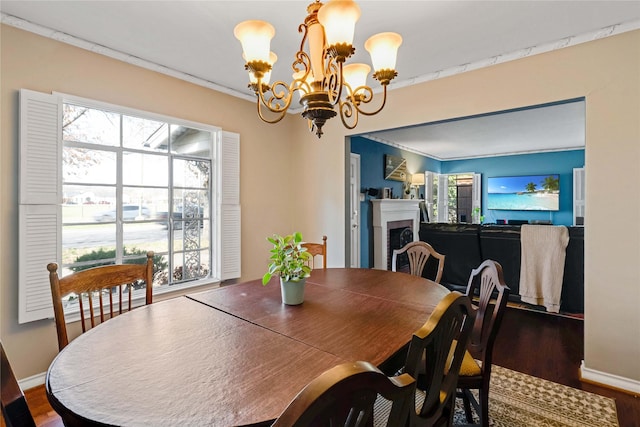 dining room with baseboards, a notable chandelier, wood finished floors, and a fireplace